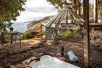 A glass-domed hut and adjacent outdoor bathtub overlook the Pacific Ocean.