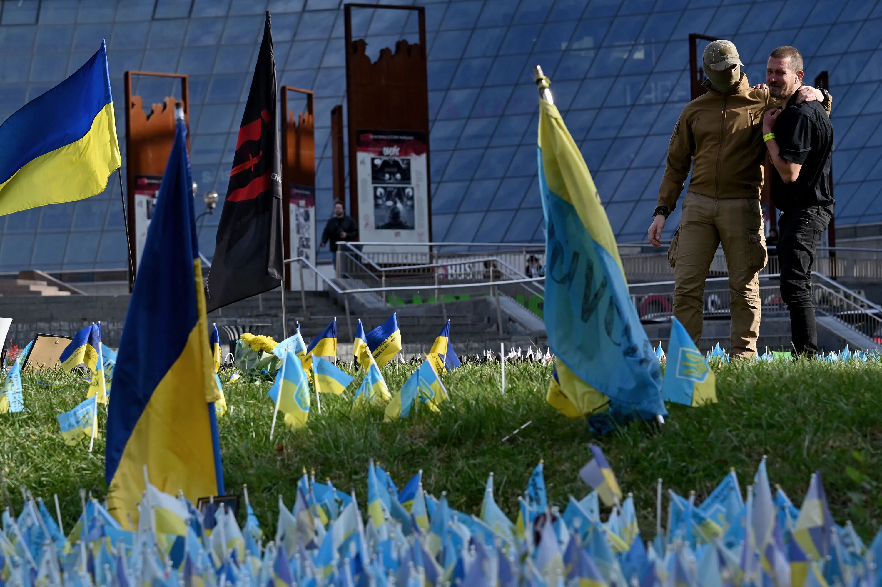 A serviceman and his friend pay tribute to comrades next to Ukrainian flags&nbsp;in Kyiv, Ukraine.