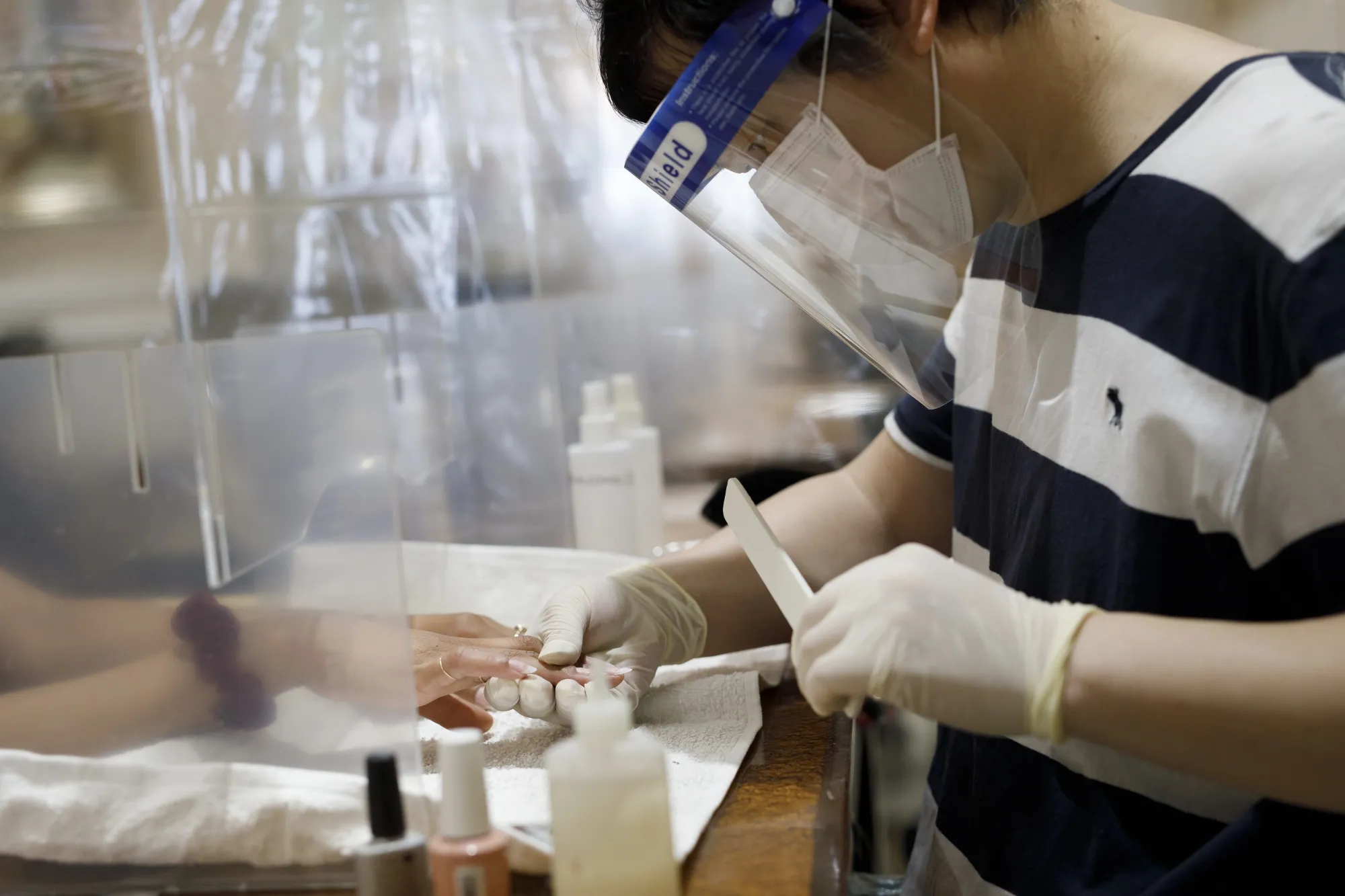A worker wearing a protective mask and face shield gives a customer a manicure at a Toronto nail salon on June 24.
