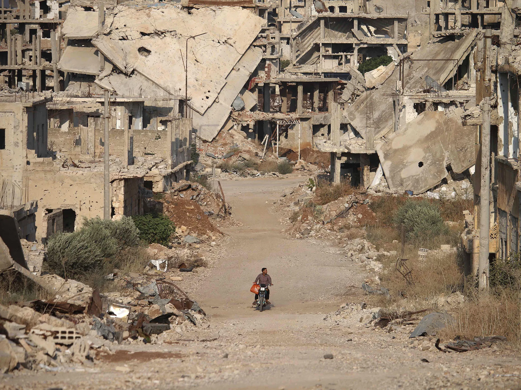 A man rides a motorcycle past destroyed buildings in the city of Daraa on Aug.&nbsp;2, 2018.