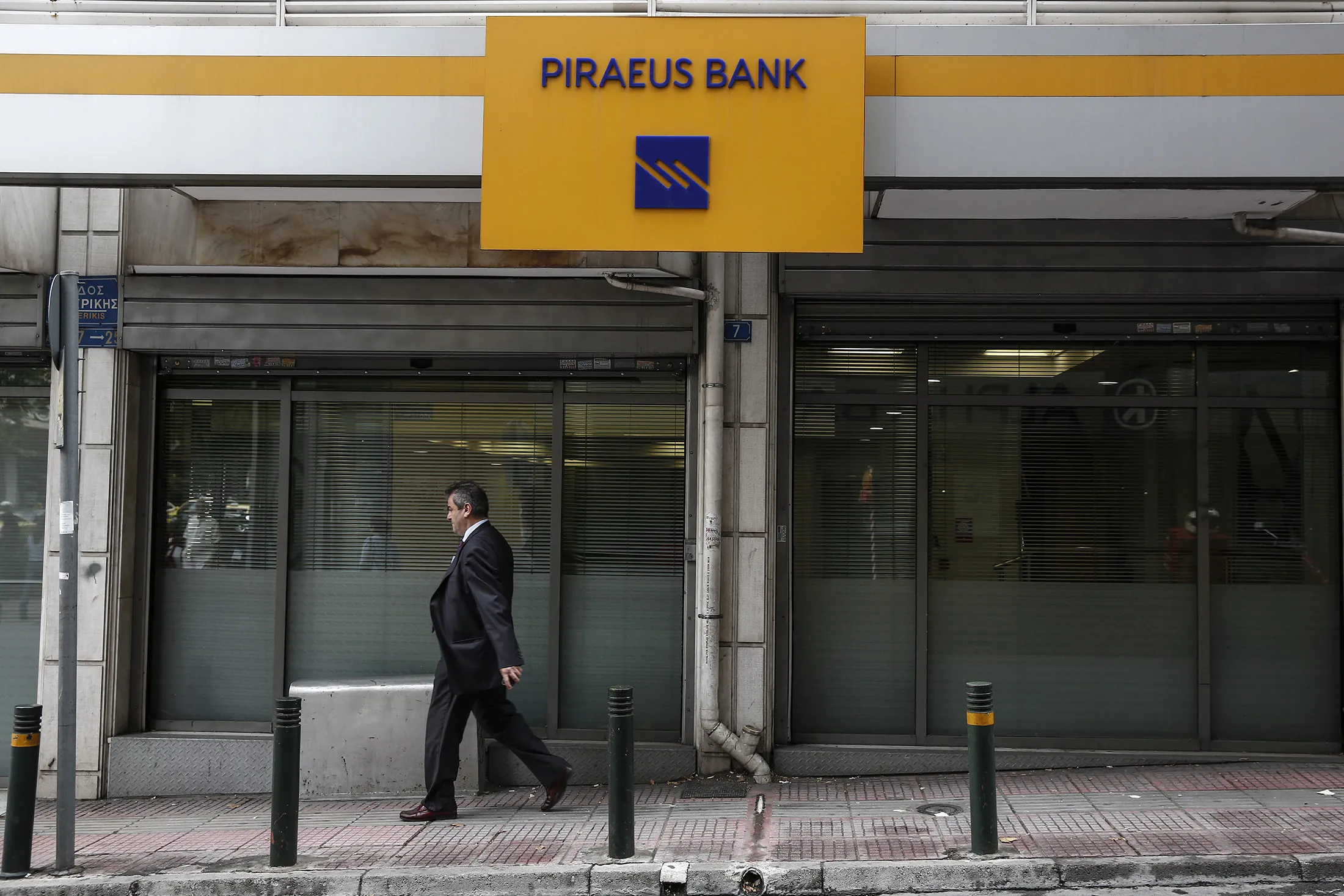 A pedestrian passes the windows of a Piraeus Bank SA bank branch in Athens.
