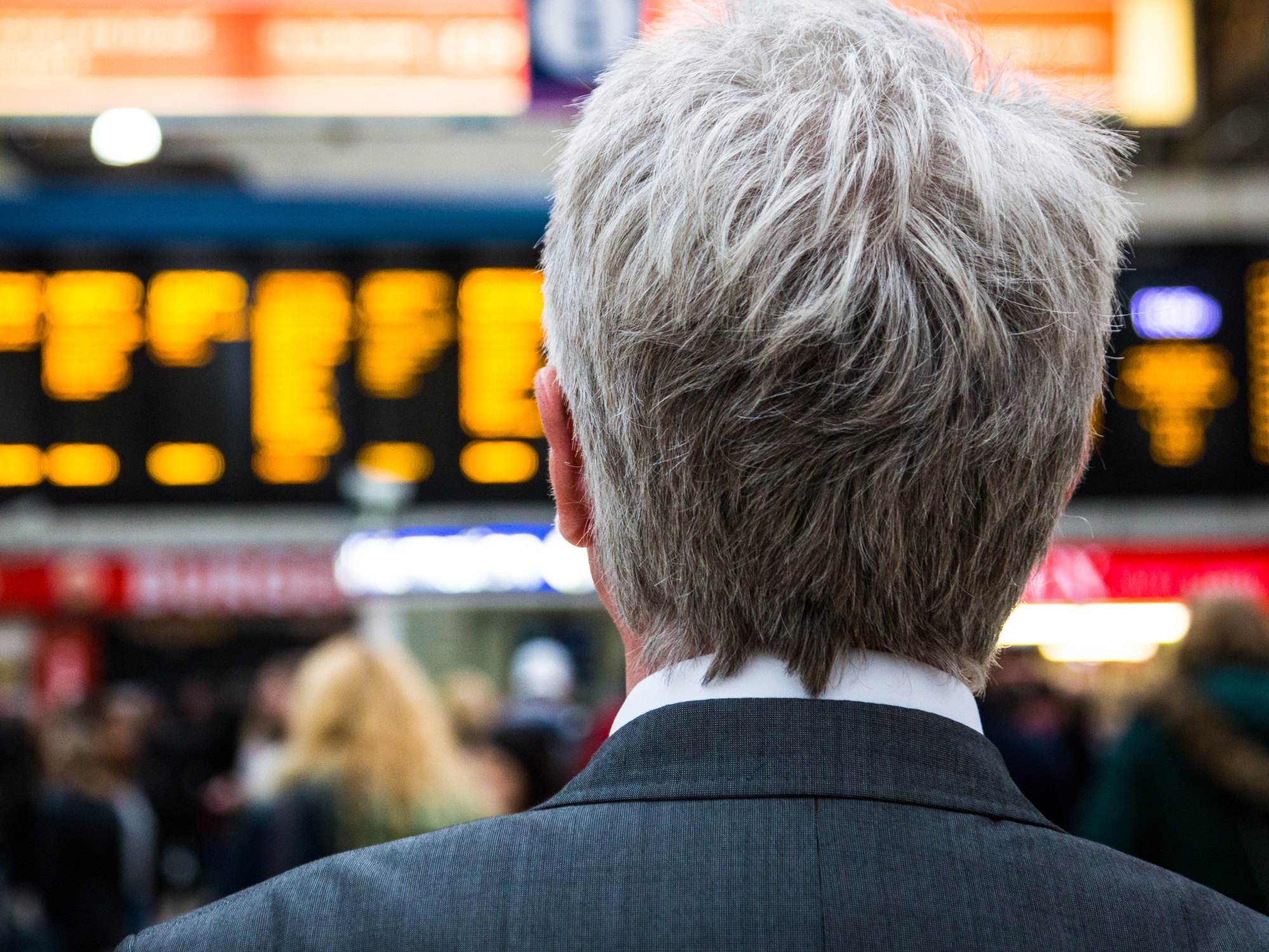 Senior businessman waiting for train with departure boards in background, London, UK