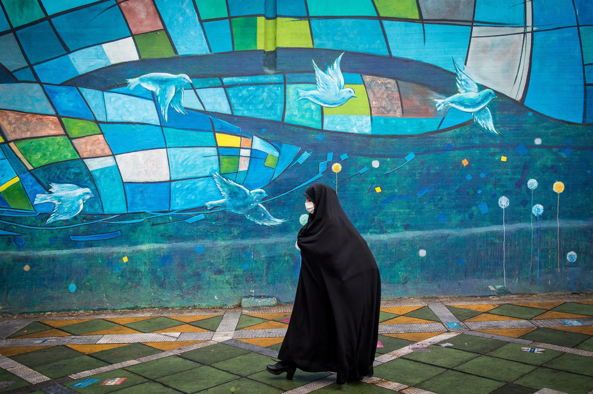 A woman wearing a chador passes a street mural in Tehran, Iran.