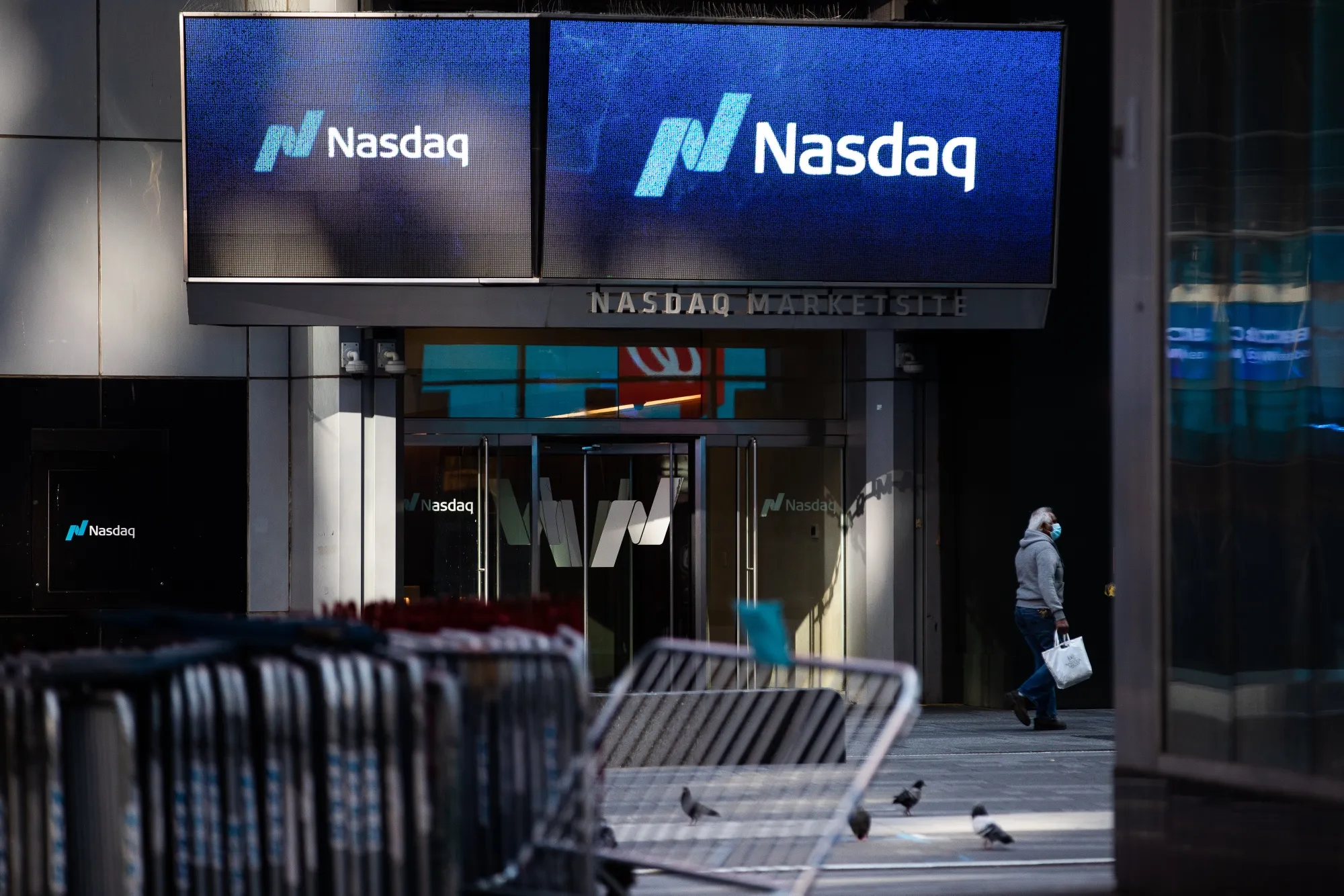 A pedestrian wearing a protective mask passes in front of the Nasdaq Market Site in Times Square.