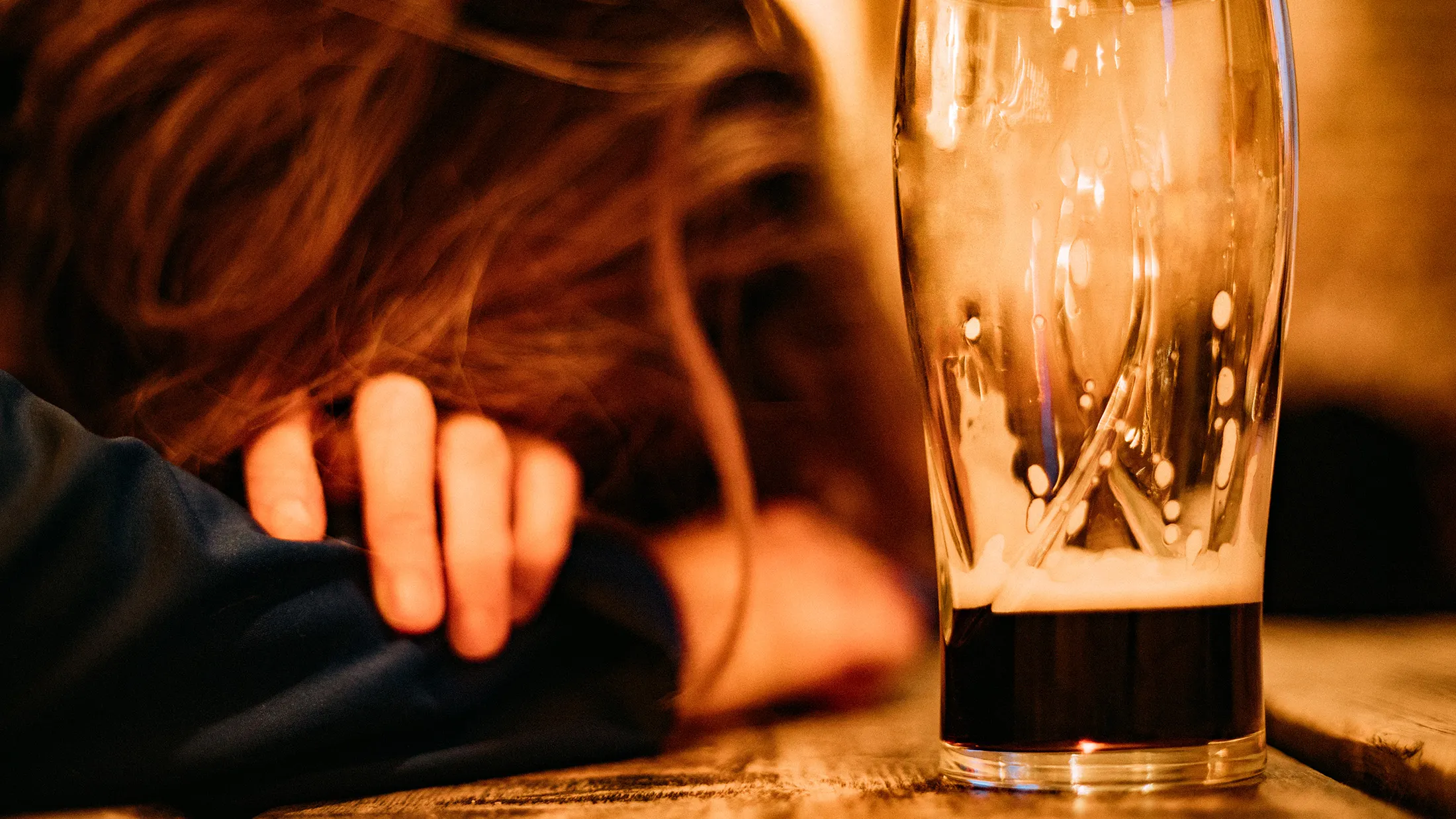Young drunk woman sleeping on bar counter drinking dark beer