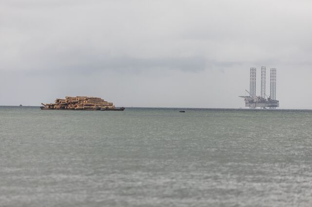 A boat transporting logs passes bay an oil rig in the Cape Lopez bay in Port-Gentil on October 14, 2022.