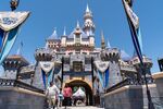 Guests wearing protective masks cross the bridge in front of Sleeping Beauty Castle during the reopening of the Disneyland theme park in Anaheim, California, U.S., on Friday, April 30, 2021. 