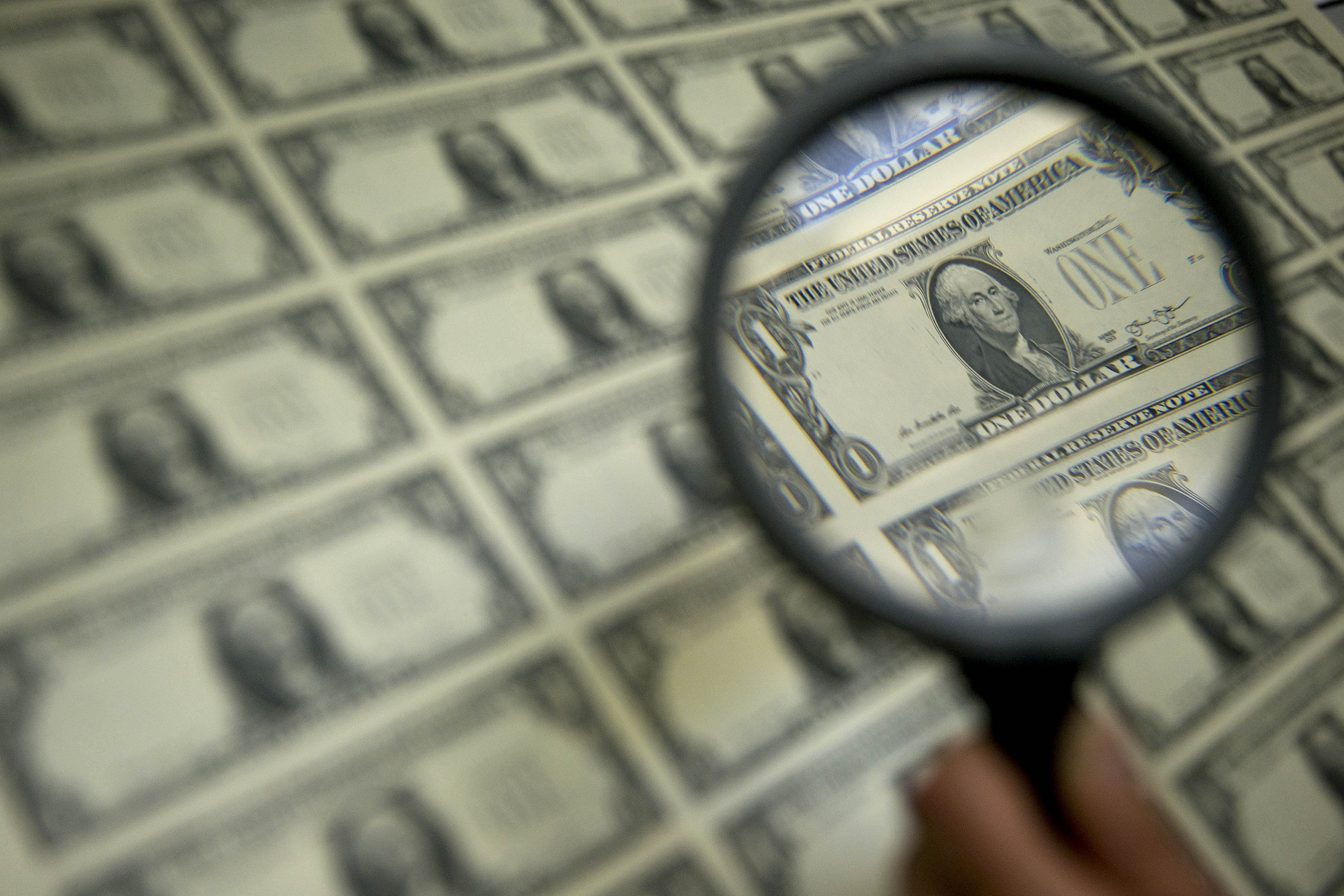 A magnifying glass is held over a 50 subject one dollar note sheet after being printed by an intaglio printing press in this arranged photograph at the U.S. Bureau of Engraving and Printing in Washington, D.C., U.S., on Tuesday, April 14, 2015.
