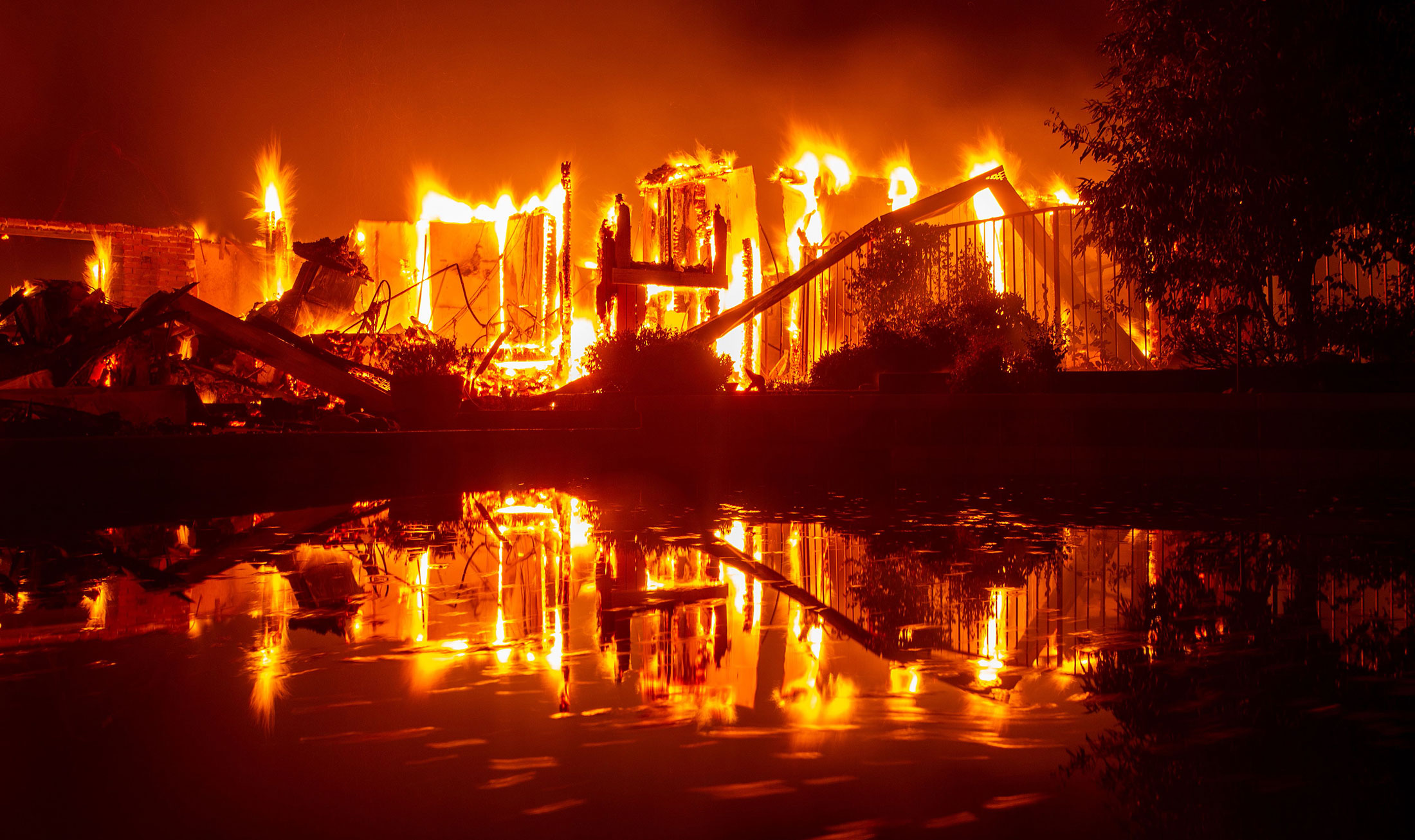 A burning home is reflected in a pool during fires in Redding, California o...