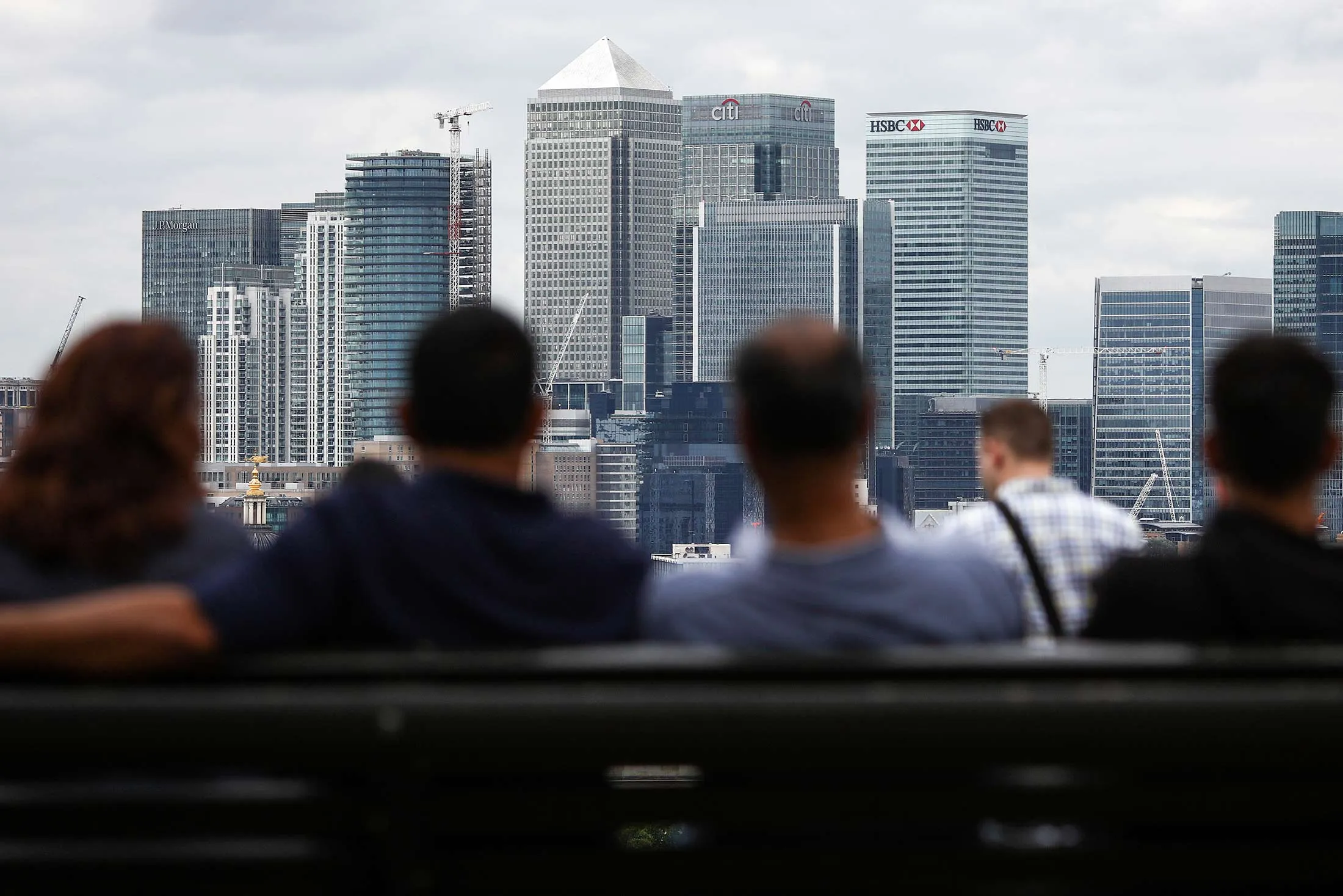 Pedestrians look at the view of the Canary Wharf financial, shopping and business district, from Greenwich Park in London.
