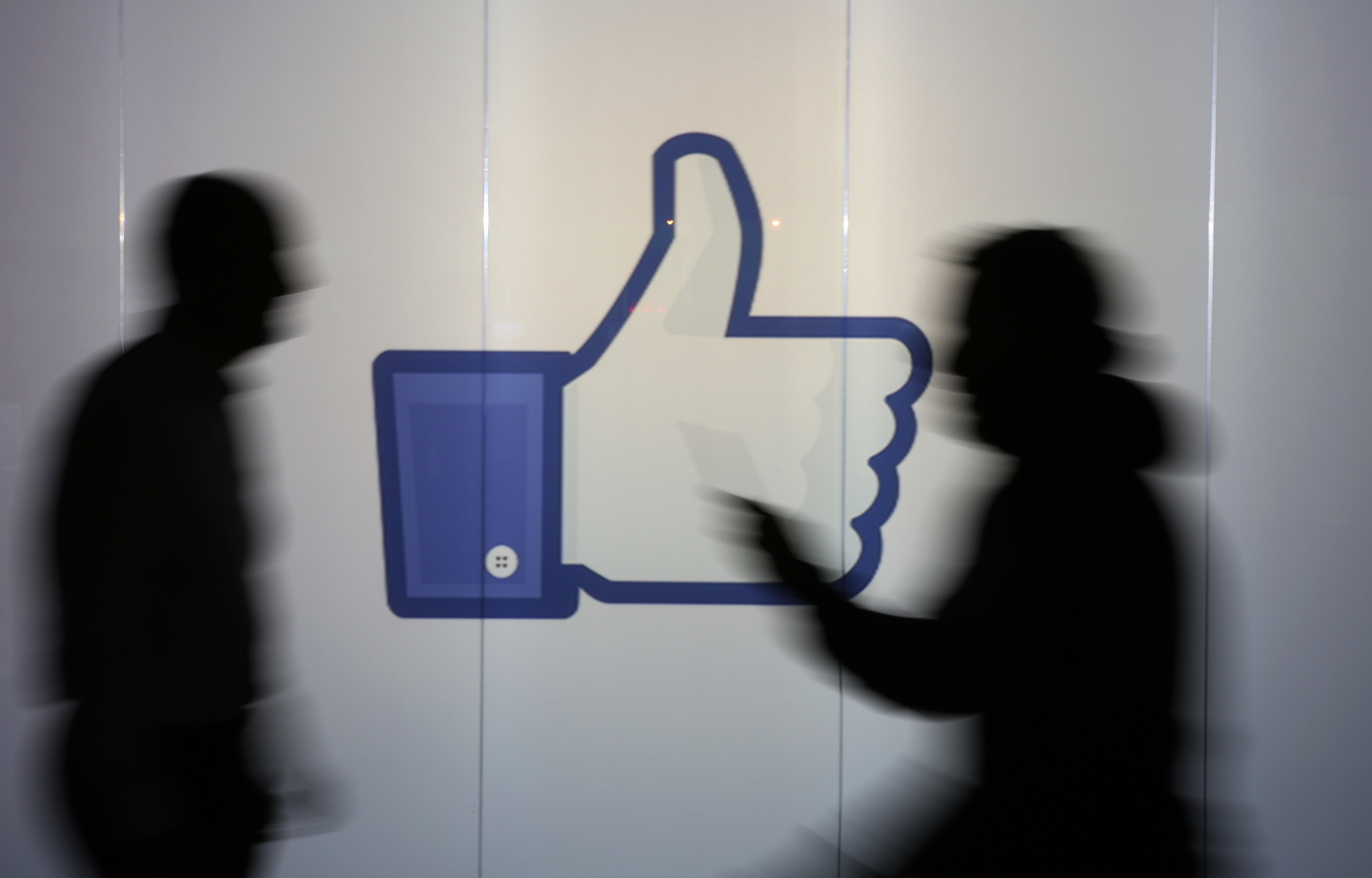 People are seen as silhouettes as they move past an illuminated wall bearing Facebook Inc.s 'Thumbs Up' symbol in this arranged photograph in London, U.K., on Wednesday, Dec. 23, 2015.