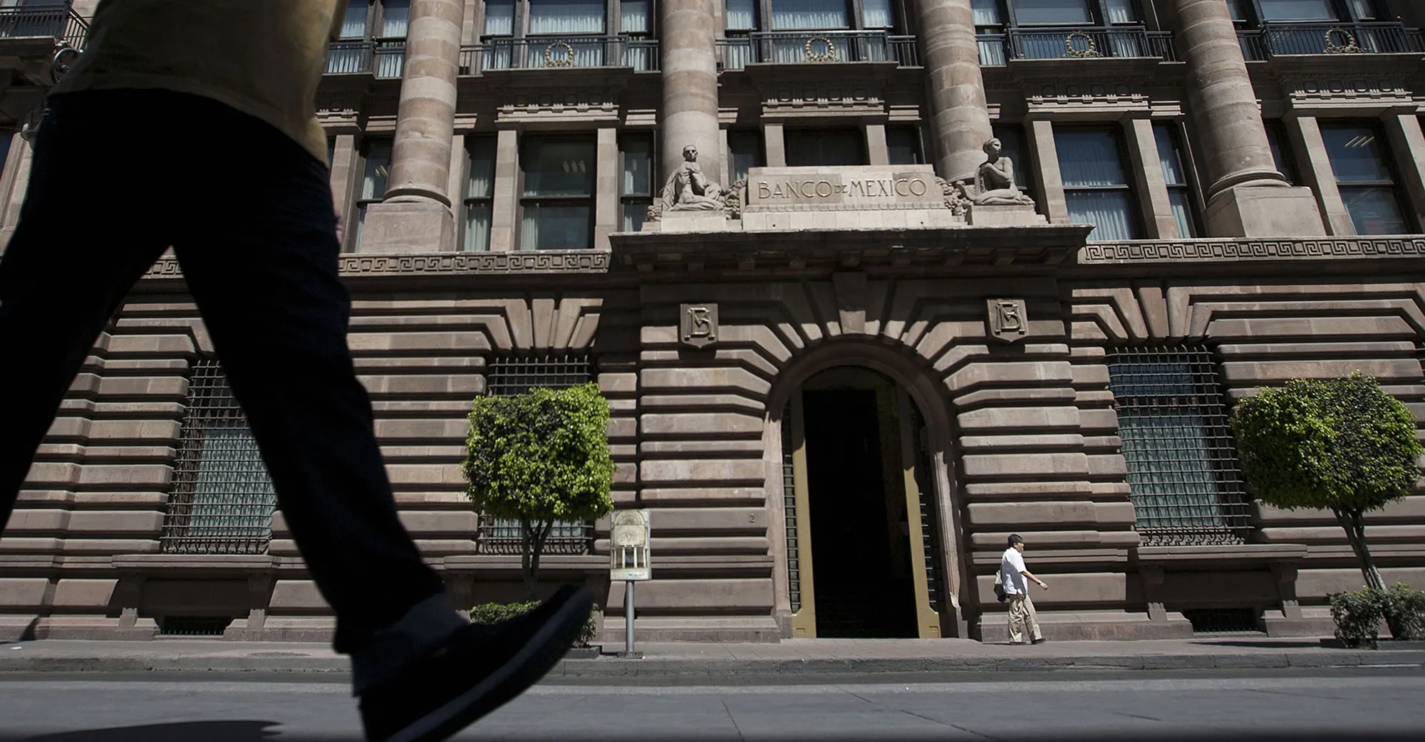 Pedestrians walk in front of the Banco de Mexico building in Mexico City.