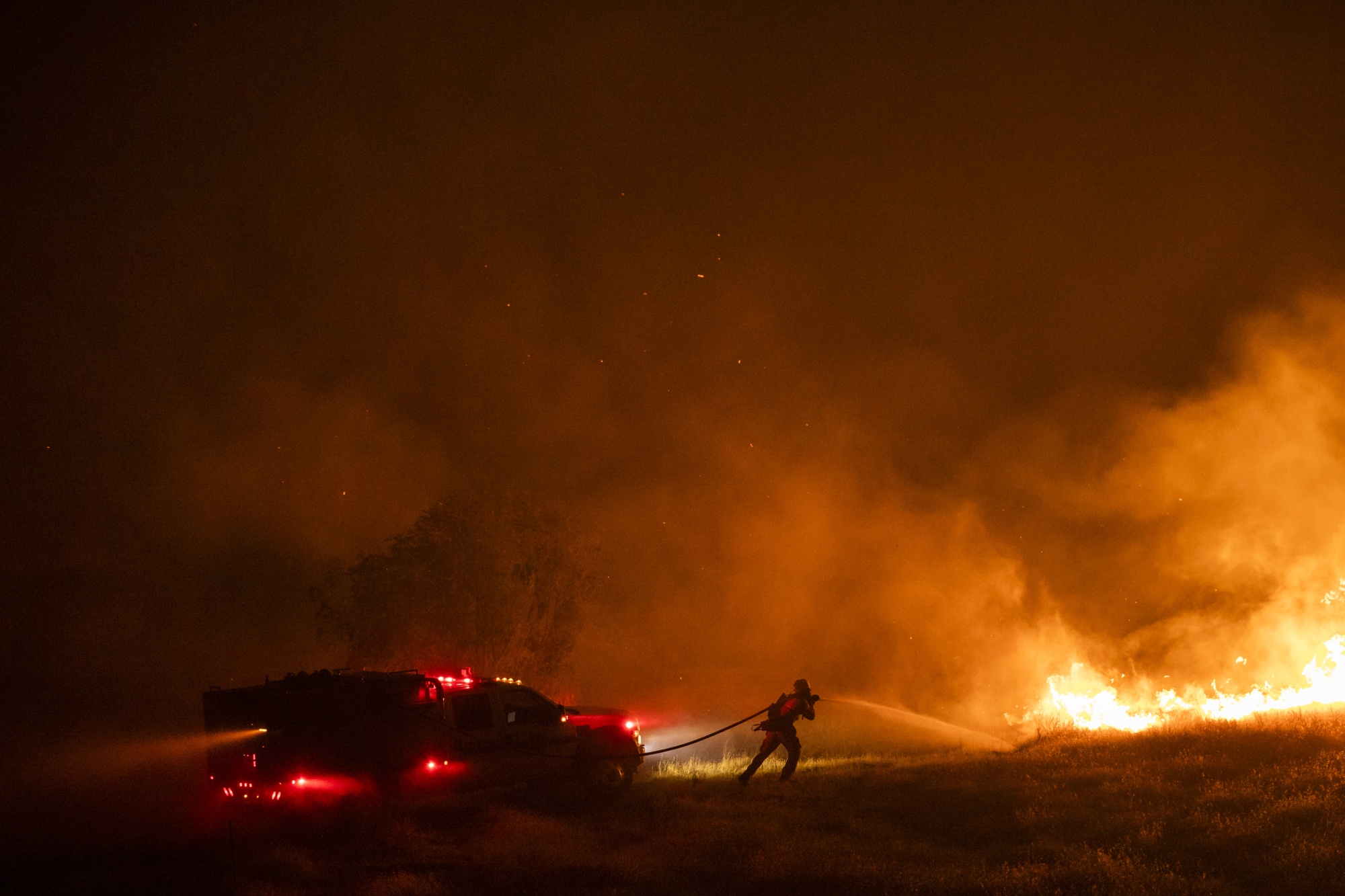 A firefighter douses flames burning on a property off Cantelow Road during the Hennessey fire in Solano County, California, U.S., on Wednesday, Aug. 19, 2020. More Northern Californians were chased out of their homes by lightning-sparked wildfires that burned out of control in several counties amid a punishing heat wave that pushed temperatures into the triple digits.
