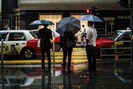 Pedestrians holding umbrellas wait to cross a road in front of a Prada SpA luxury fashion store in the Central district of Hong Kong, China, on Wednesday, April 13, 2016. When Prada on Monday outlined plans to rekindle growth, marketing chief Stefano Cantino boasted that the Italian luxury-goods maker still "sets the trend in the industry." Unfortunately for Prada's investors, it's a leader in the wrong metrics. Photographer: Billy H.C. Kwok/Bloomberg