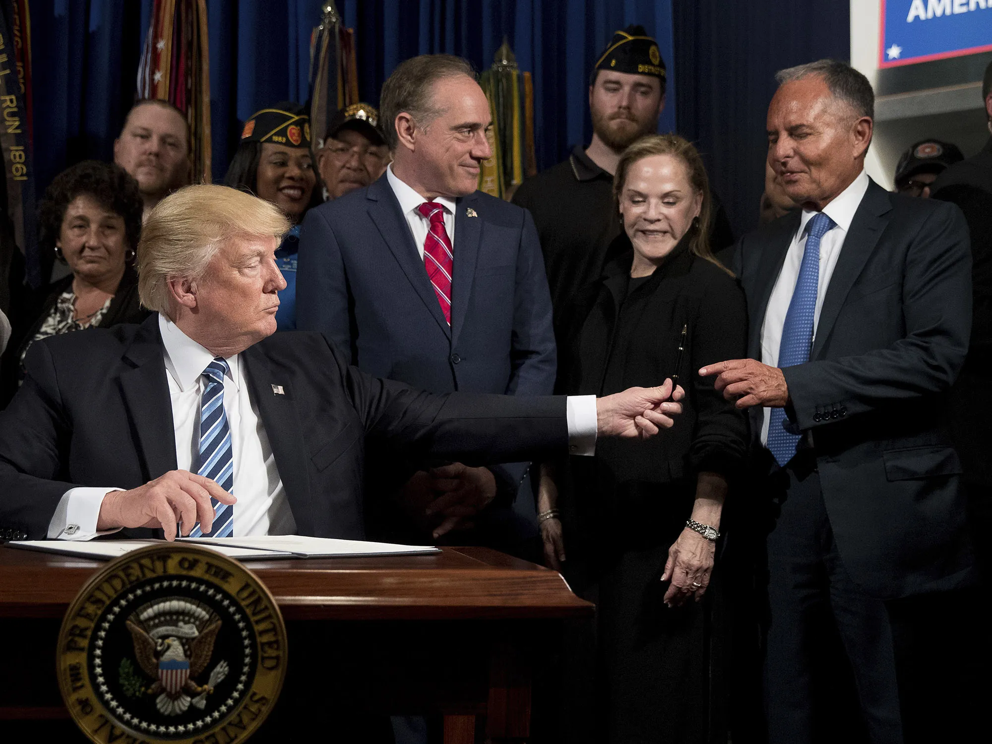 Donald Trump hands his pen to Isaac Perlmutter after signing an Executive Order in 2017. Laura Perlmutter stands next to her husband at second right.  