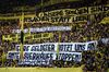 Fans standing in a football stadium holding banners in German