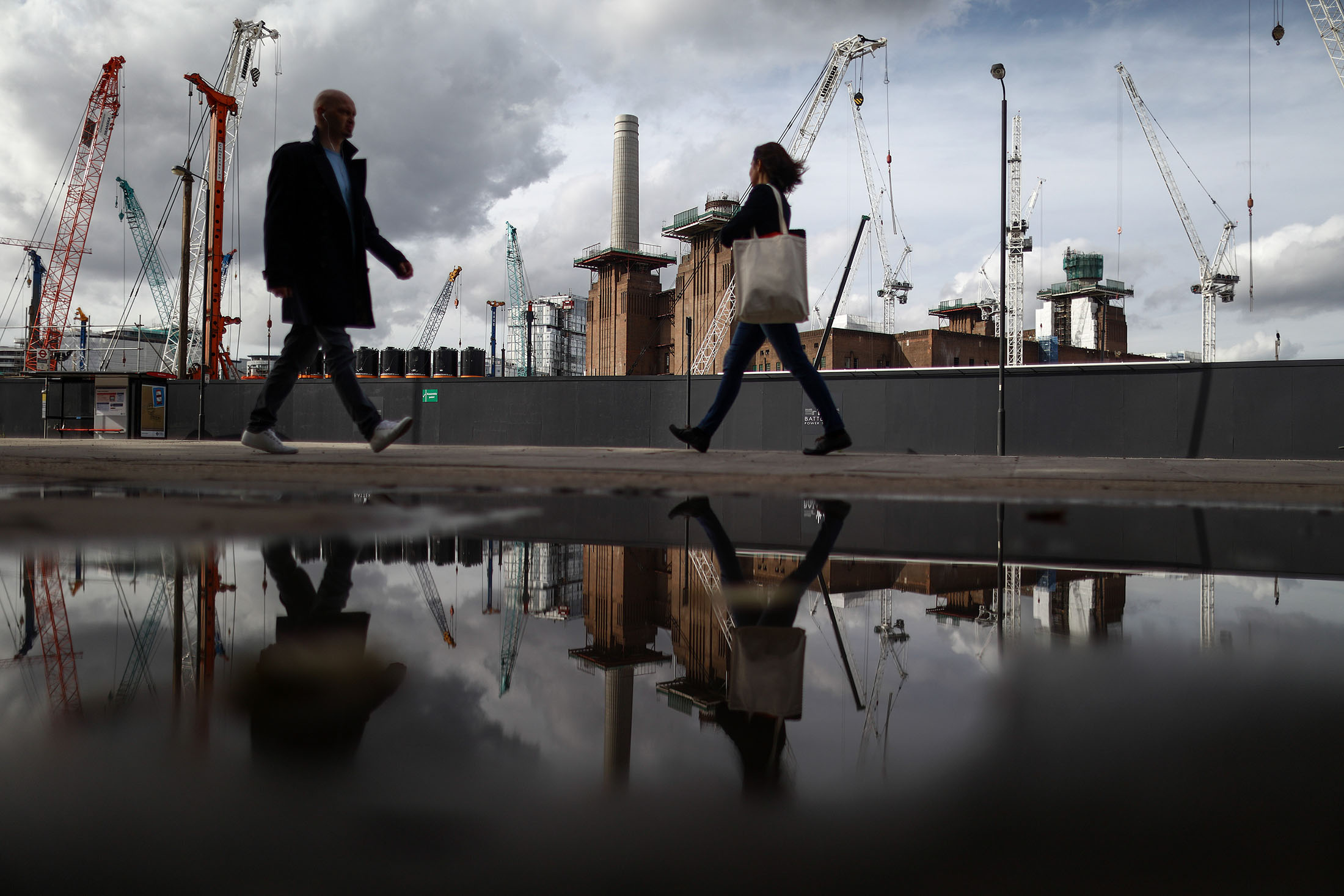Pedestrians walk past construction cranes at the Battersea Power Station office.&nbsp;