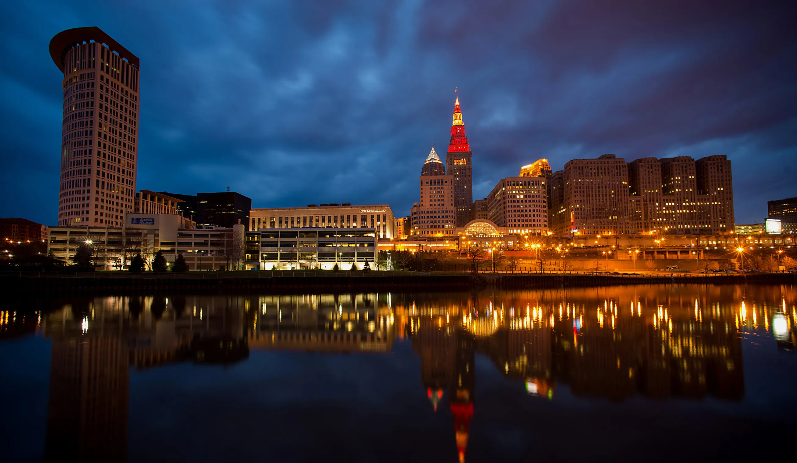 Buildings standing in the downtown skyline are reflected in the Cuyahoga River in Cleveland, Ohio, U.S., on Saturday, April 12, 2014. Demand for manufactured products in Cleveland grew at a slow rate as building contractors reported that pipelines remained active while field work slowed, according to an April 16 U.S. Federal Reserve report.
