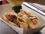 Spicy mustard is added to a dog with chili next to another dog with chili and horseradish sauce at D