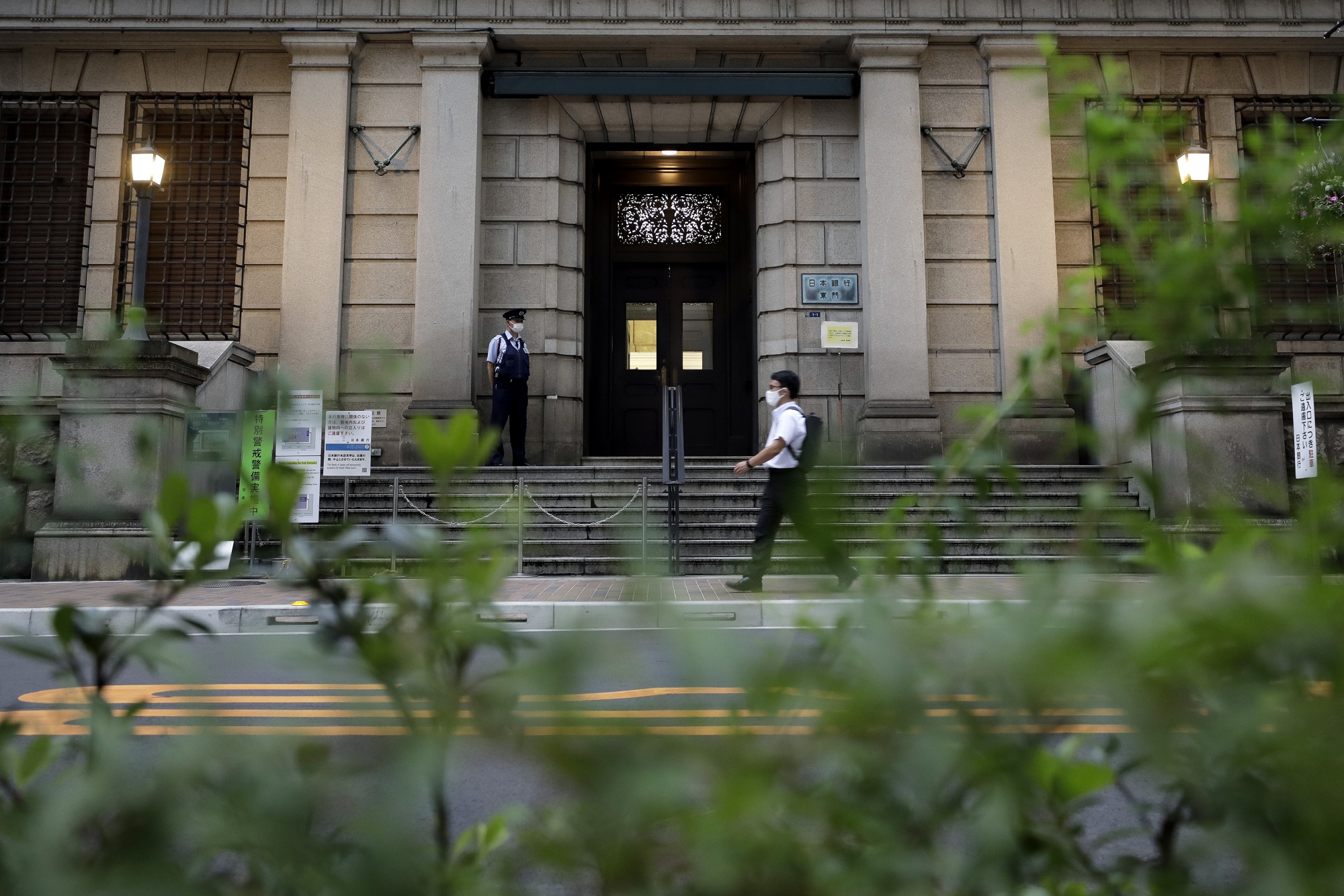 A security guard wearing a protective mask, left, stands outside the Bank of Japan (BOJ) headquarters in Tokyo, Japan, on Monday, September 14, 2020. The Bank of Japan dropped the purchase amount of unchanged bonds in a regular trade.  Monday.