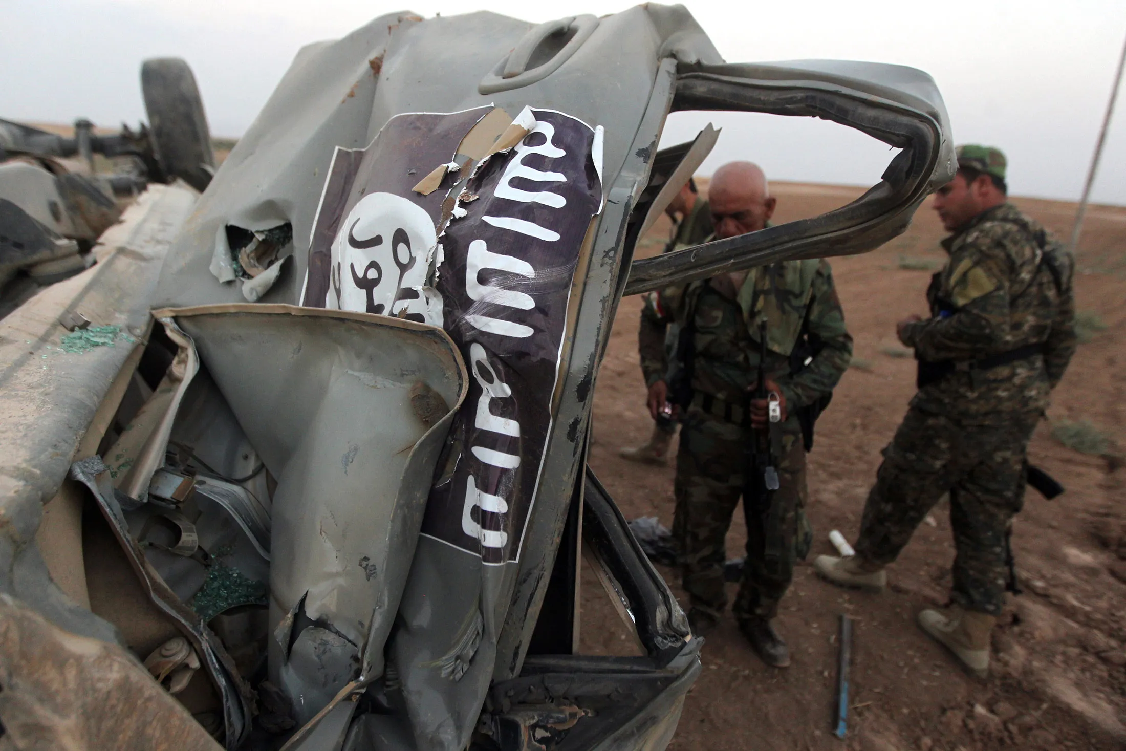 Peshmerga fighters inspect the remains of a car, bearing an image of the trademark jihadist flag, which belonged to Islamic State (IS) militants after it was targeted by an American air strike in the village of Baqufa, north of Mosul, on August 18, 2014.
