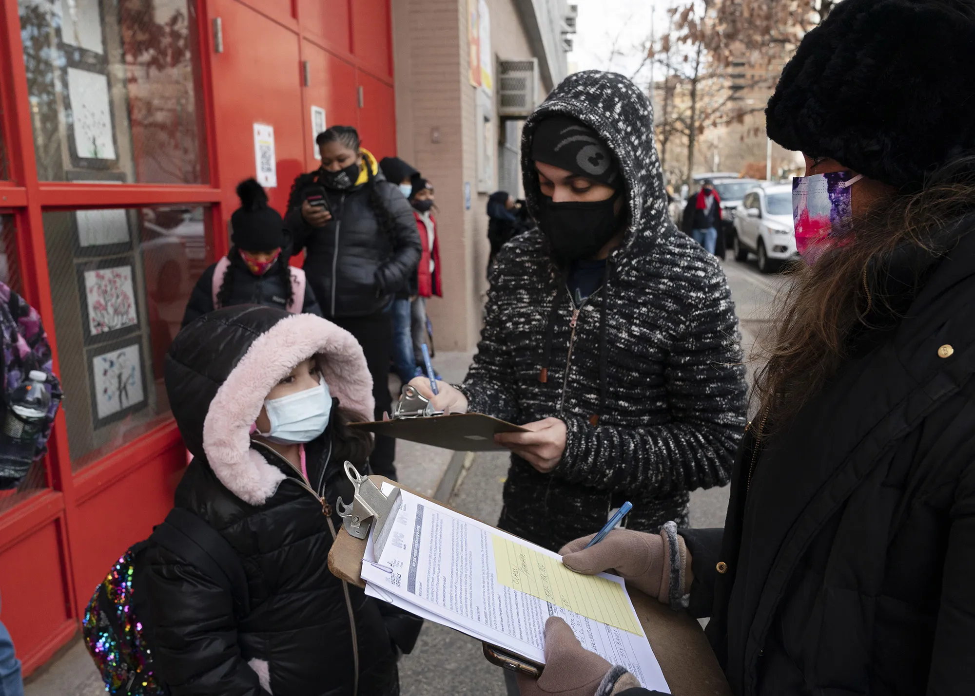 A parent, center, completes a form granting permission for random student Covid-19 testing as he arrives with his daughter at an elementary School in New York on Dec. 7.