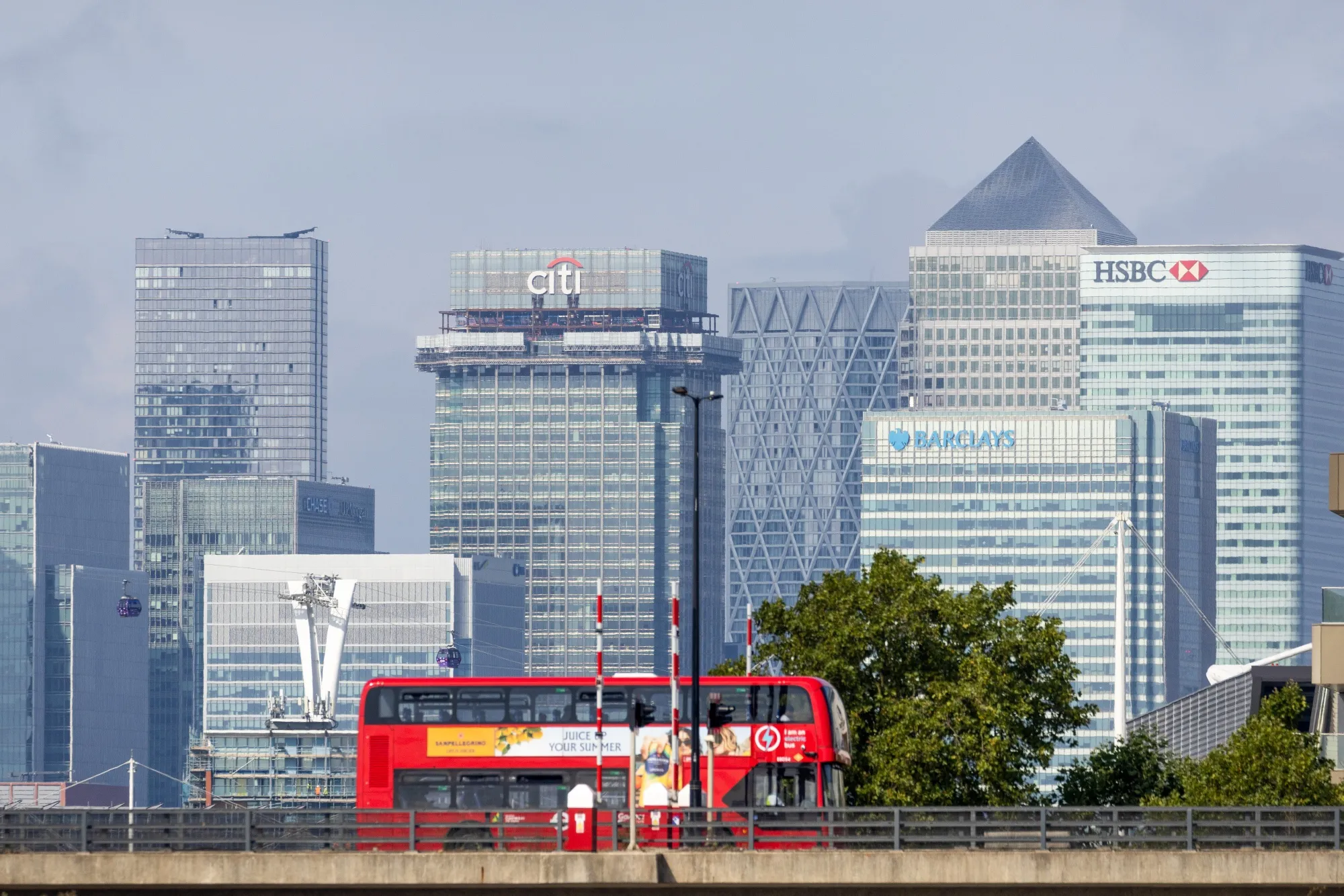 A London bus crosses a bridge near to London City Airport Ltd. in view of the Canary Wharf business, financial and shopping district, in London, UK.