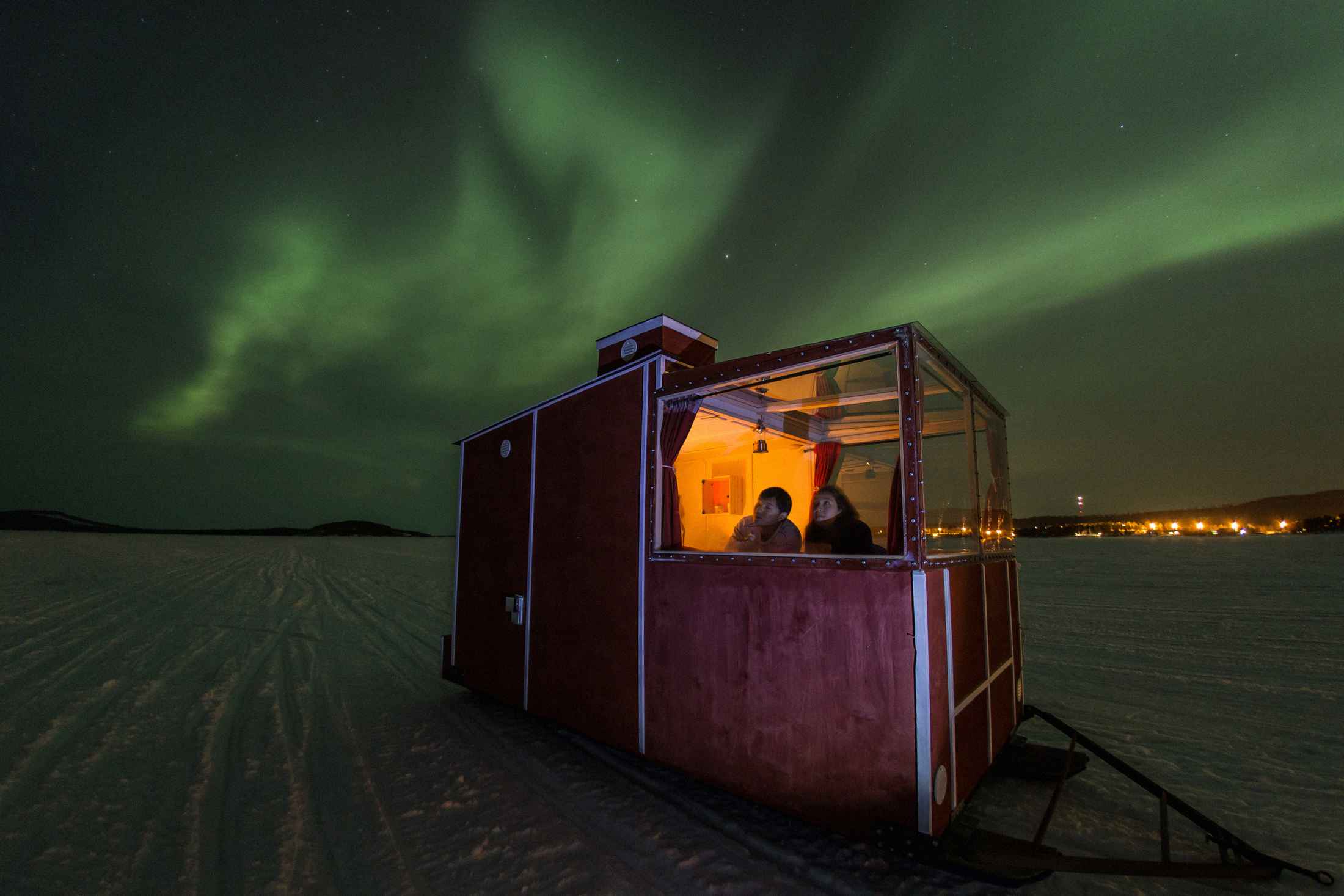A couple gazes up at the northern lights from a mobile cabin on Finland’s Lake Inari.