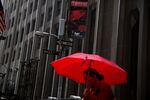 A woman carries a red umbrella while walking along Wall Street near the New York Stock Exchange.