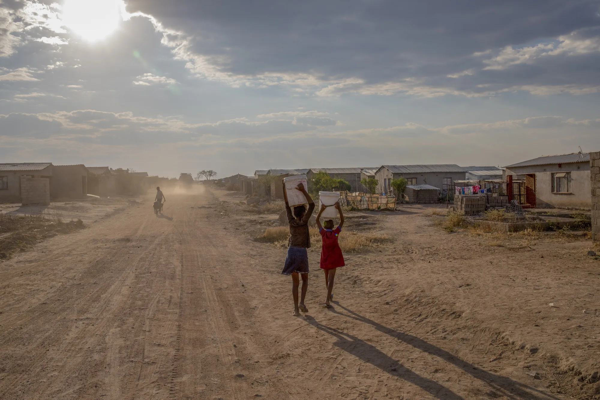 Children carry water from a communal tap in Empopini, Cowdray Park, Bulawayo, Zimbabwe.