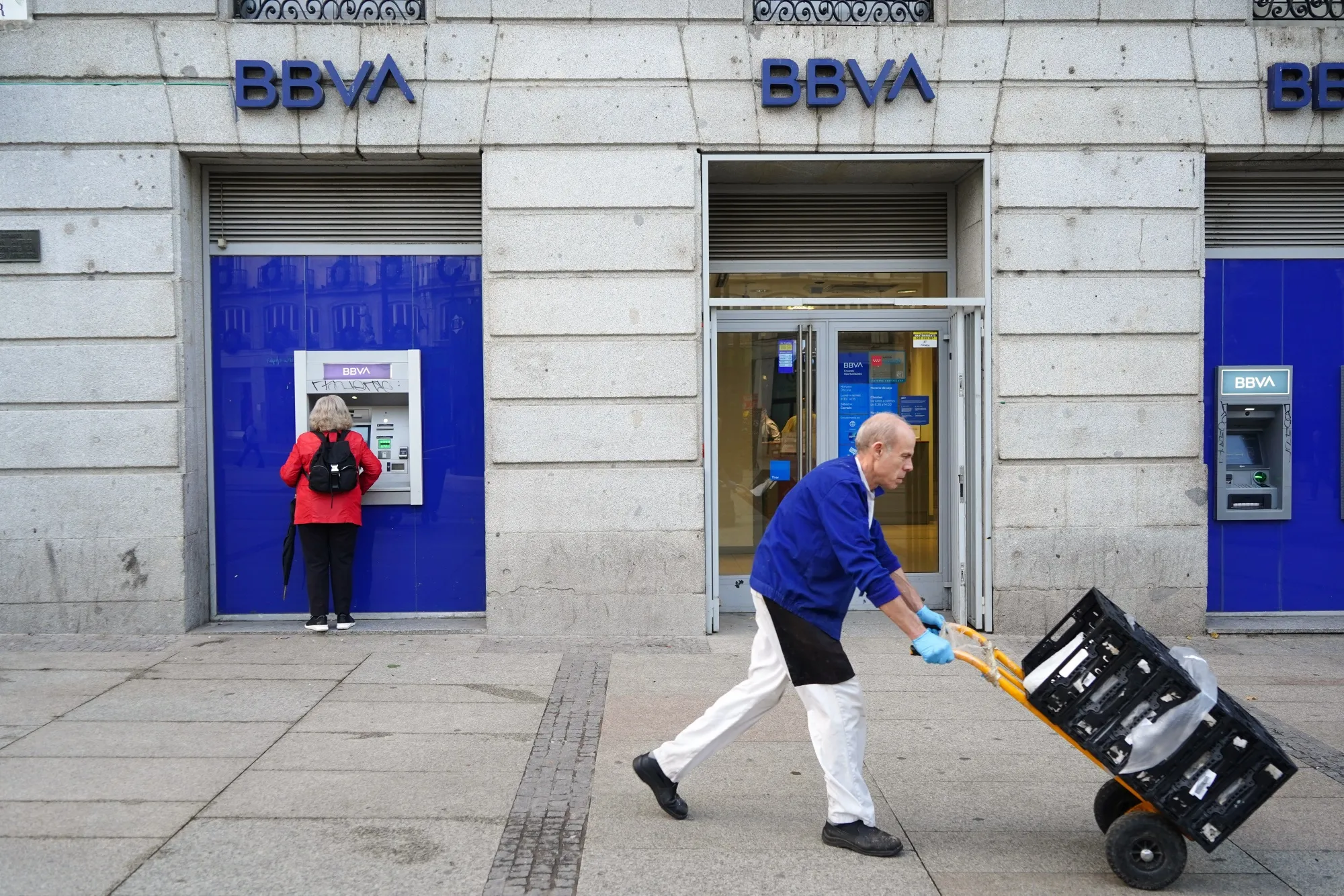 A delivery worker wheels a trolley past a BBVA bank branch in Madrid.