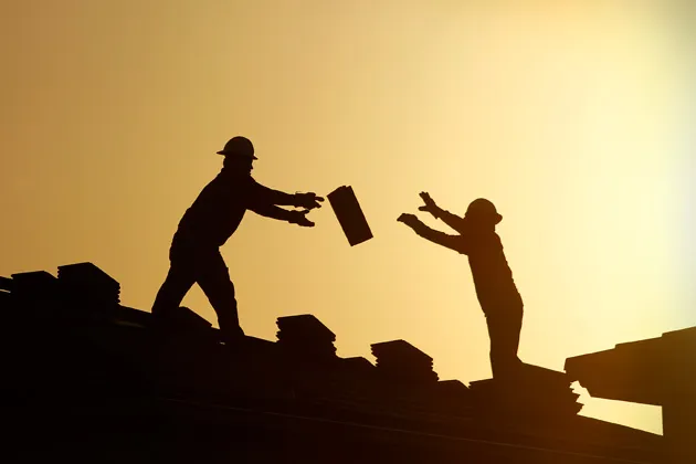 Construction workers pass a bundle of shingles on the roof of a home in Phoenix