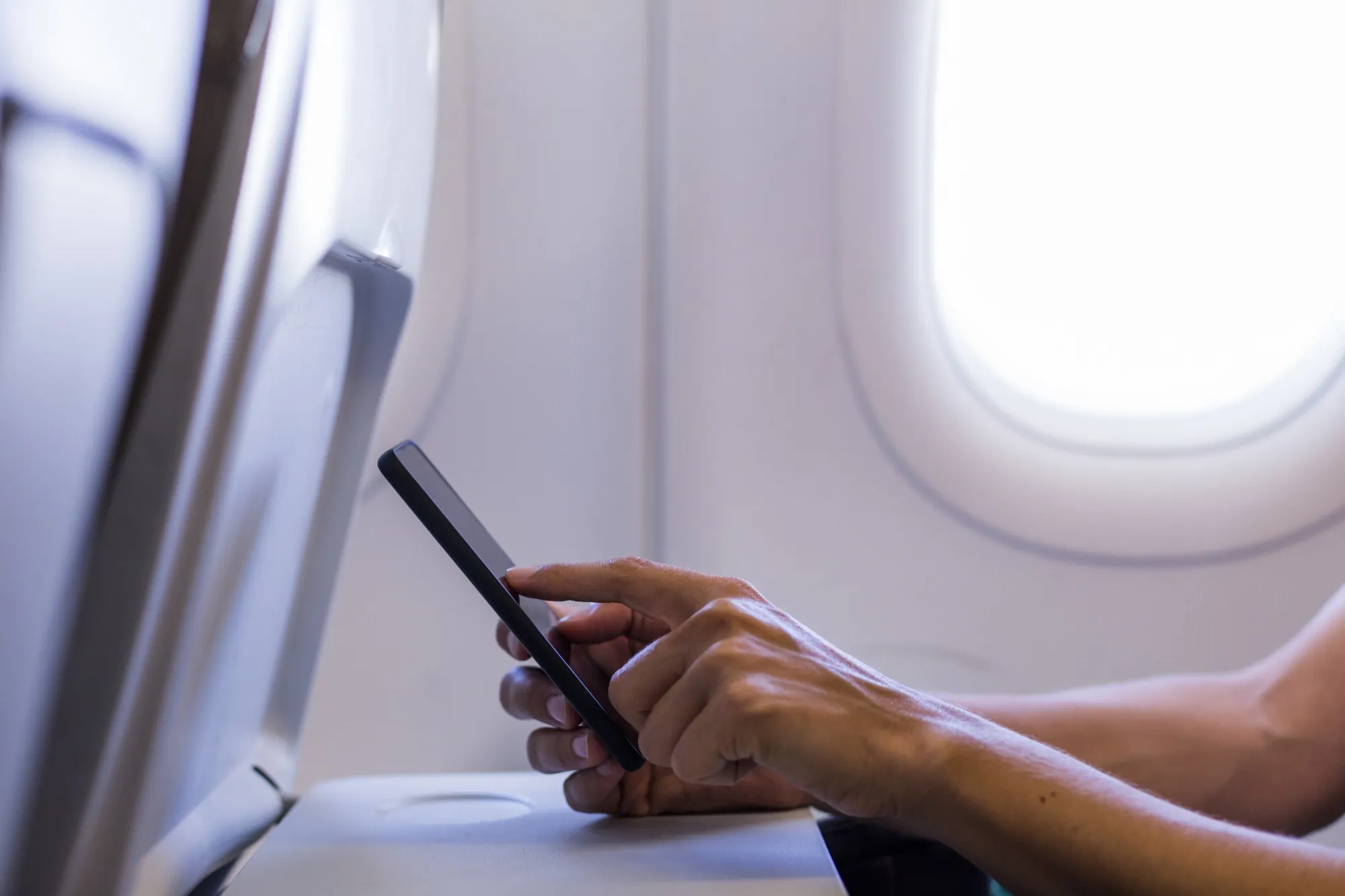 Cropped Hands Of Woman Using Mobile Phone In Airplane