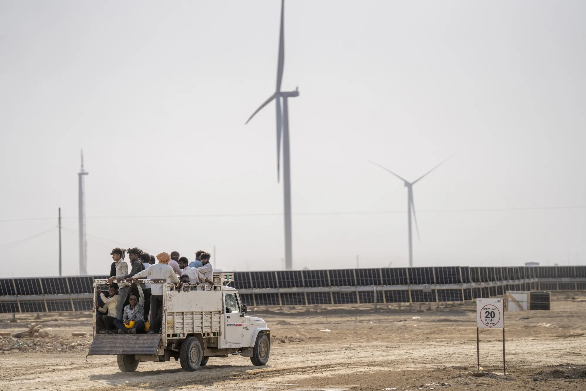 Workers drive past wind turbines and solar panels at Adani Green Energy Ltd.’s&nbsp;renewable power park in Khavda, Gujarat.