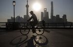 A man rides a bicycle along the Bund while buildings of Pudong's Lujiazui financial district stand across the Huangpu River as the sun rises in Shanghai, China, on Friday, Oct. 2, 2015. 