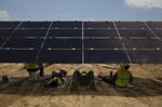 Workers take a break in the shade of a solar panel during construction of a solar generating facility in Milligan, Tennessee.