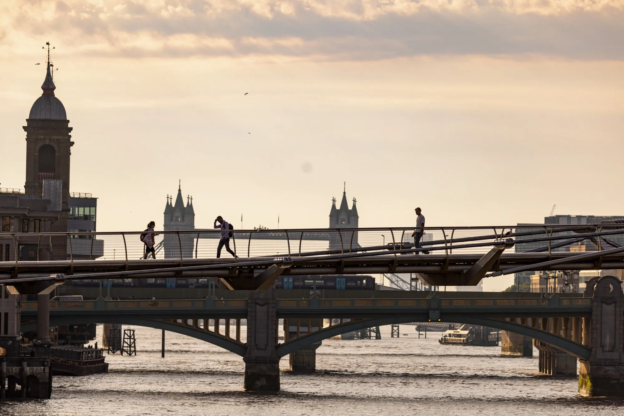 Commuters cross the Millennium Bridge in view of Tower Bridge in London, UK.