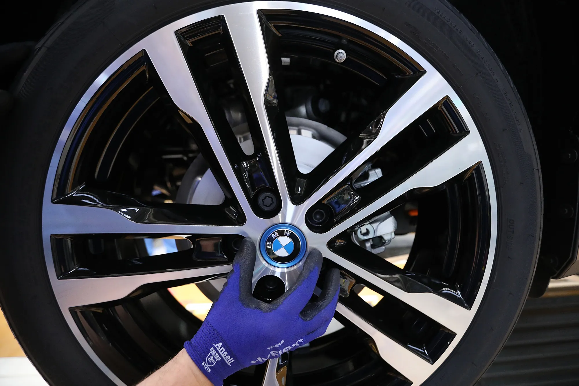 An employee fits a wheel hub badge to a BMW i3 electric automobile on the assembly line at the Bayerische Motoren Werke AG factory in Leipzig, Germany.