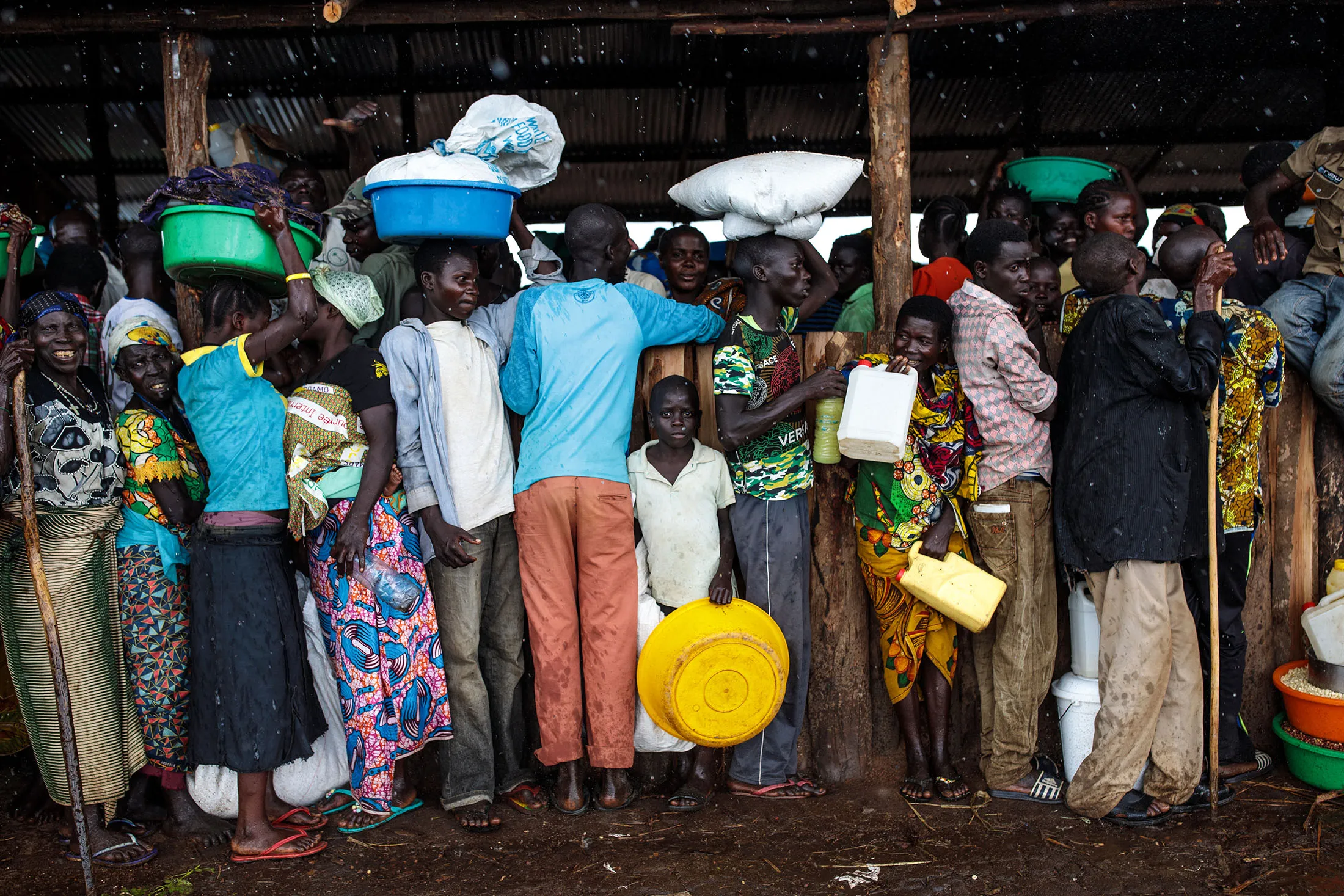 Refugees from the Democratic Republic of Congo stand under a shelter with their food collected from the World Food Programme as it rains in the Kyangwali settlement in Kyangwali, Uganda on April 10, 2018.