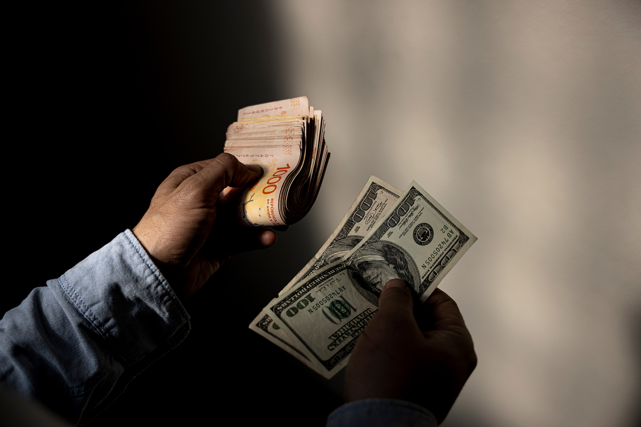 A black-market currency exchanger holds two US hundred dollar bank notes and the equivalent in 1000 peso.