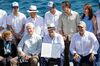 President Guillermo Lasso, center, holds the decree he signed at an event aboard a boat surrounded by people, including former U.S. President Bill Clinton