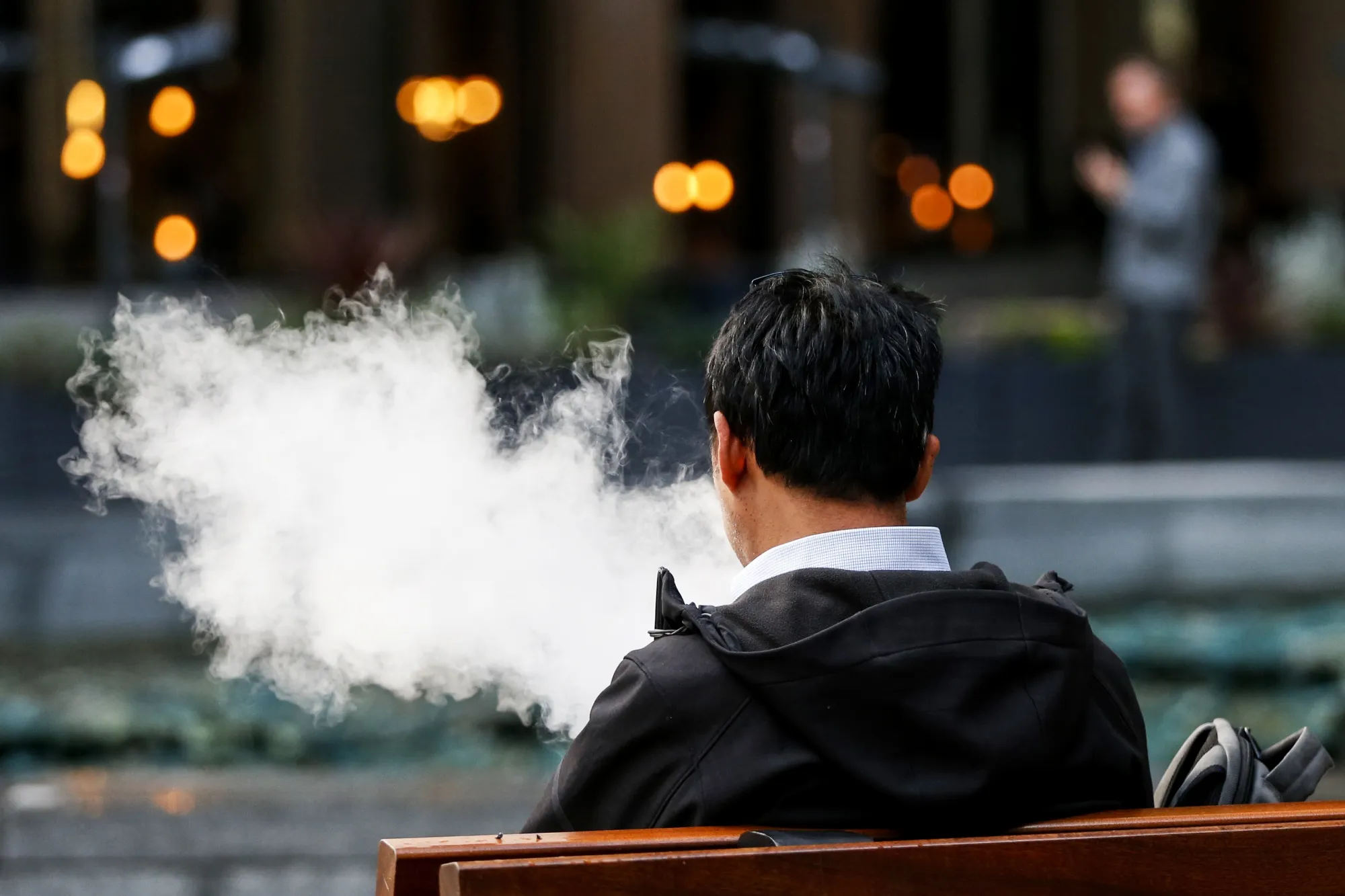 A pedestrian exhales a cloud of vapour from a vape device.
