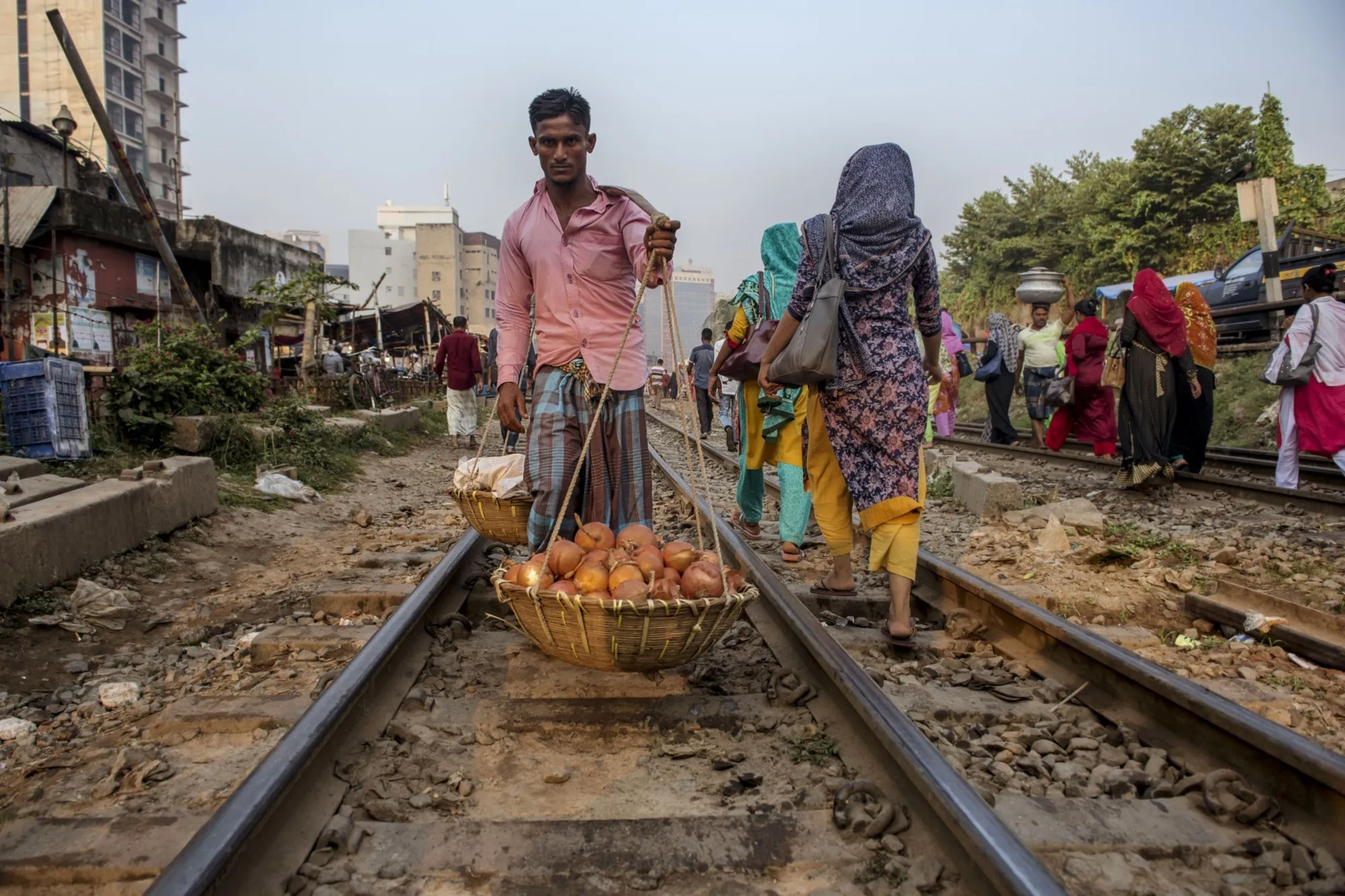A street vendor carries a basket of onions while walking along the a rail track near the Kawran Bazar in Dhaka, Bangladesh, in December 2019.