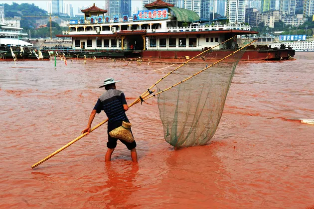 A fisherman works in the Yangtze river, which appears red in color on September 6, 2012 in Chongqing, China.