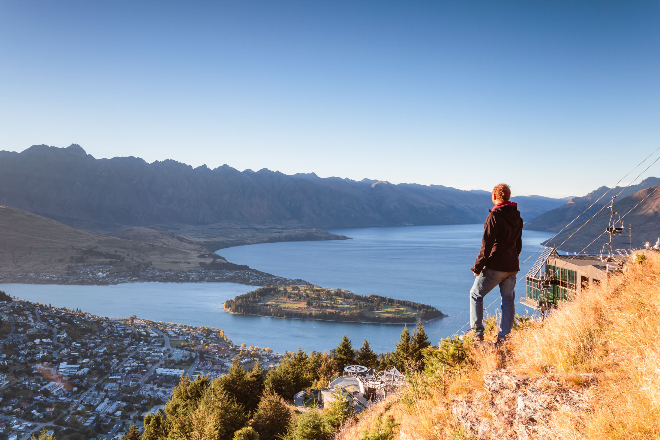 Hiker looking at Queenstown from lookout at sunrise, New Zealand