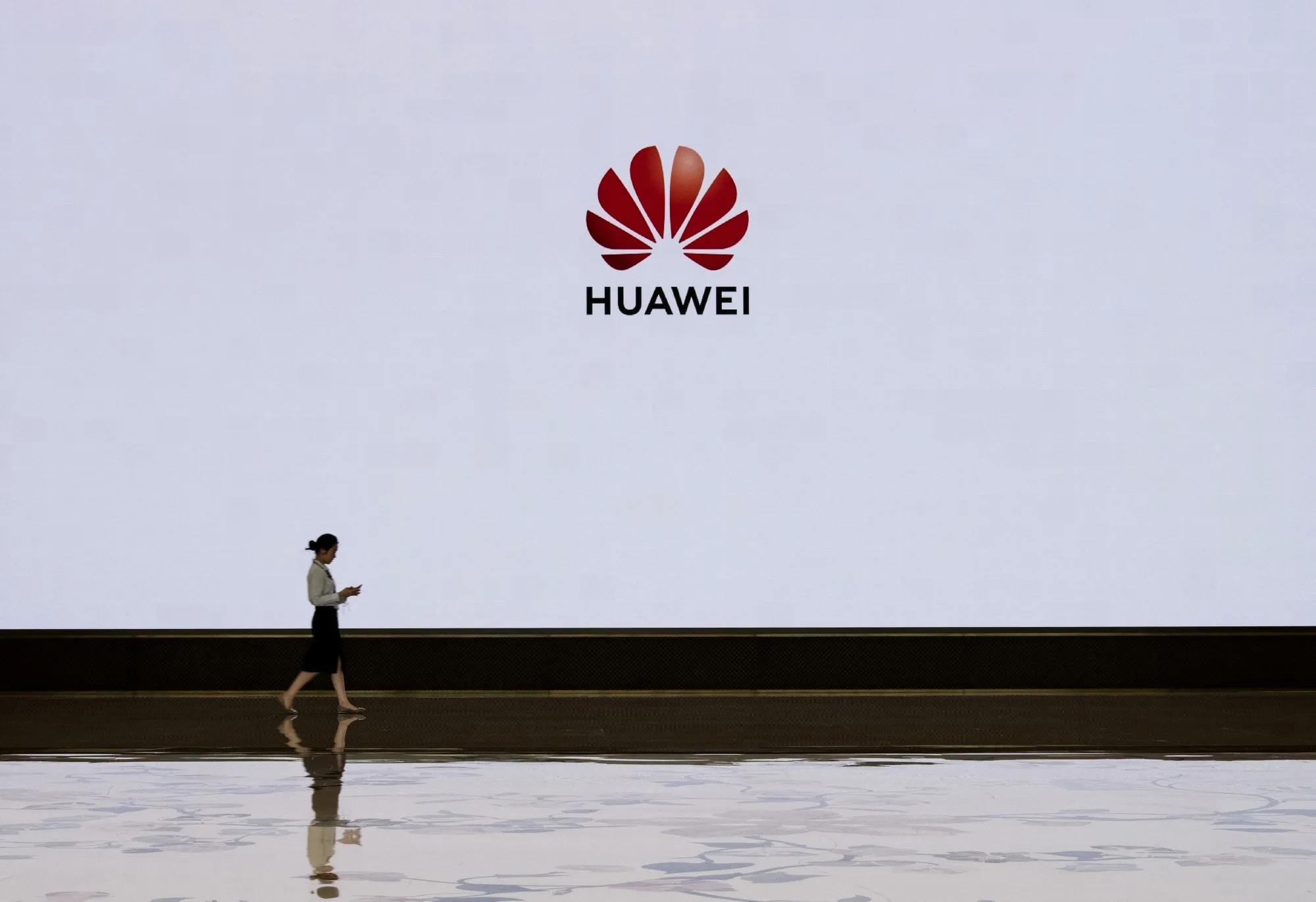 A member of Huawei's reception staff walks in front of a large screen displaying the logo in the foyer of a building used for high profile customer visits and displays at the company's Bantian campus on April 12, 2019 in Shenzhen, China. (Photo by Kevin Frayer/Getty Images)
