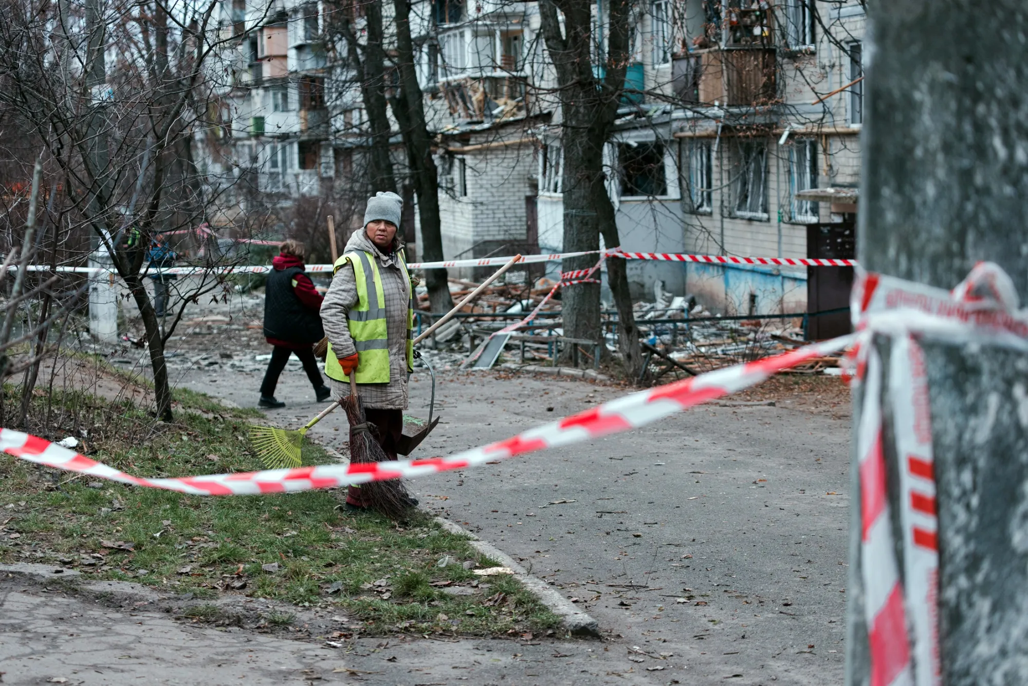 A woman helps clear debris&nbsp;near a cordoned off building damaged following a Russian attack in Kyiv, on Dec. 23.