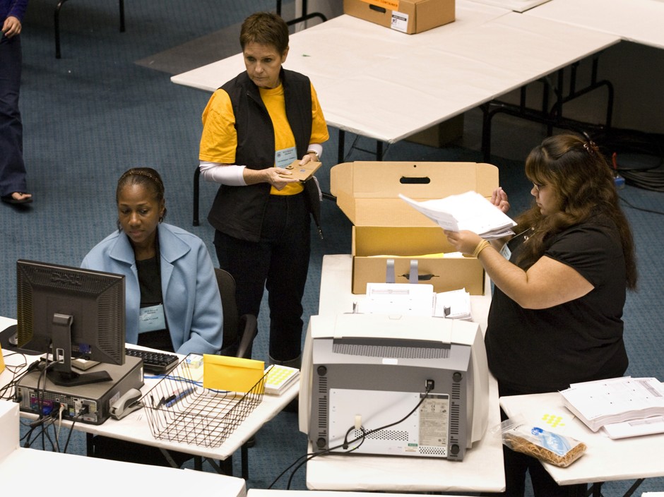 A neutral observer, top, watches as two election staffers help count absentee and mail-in ballots.