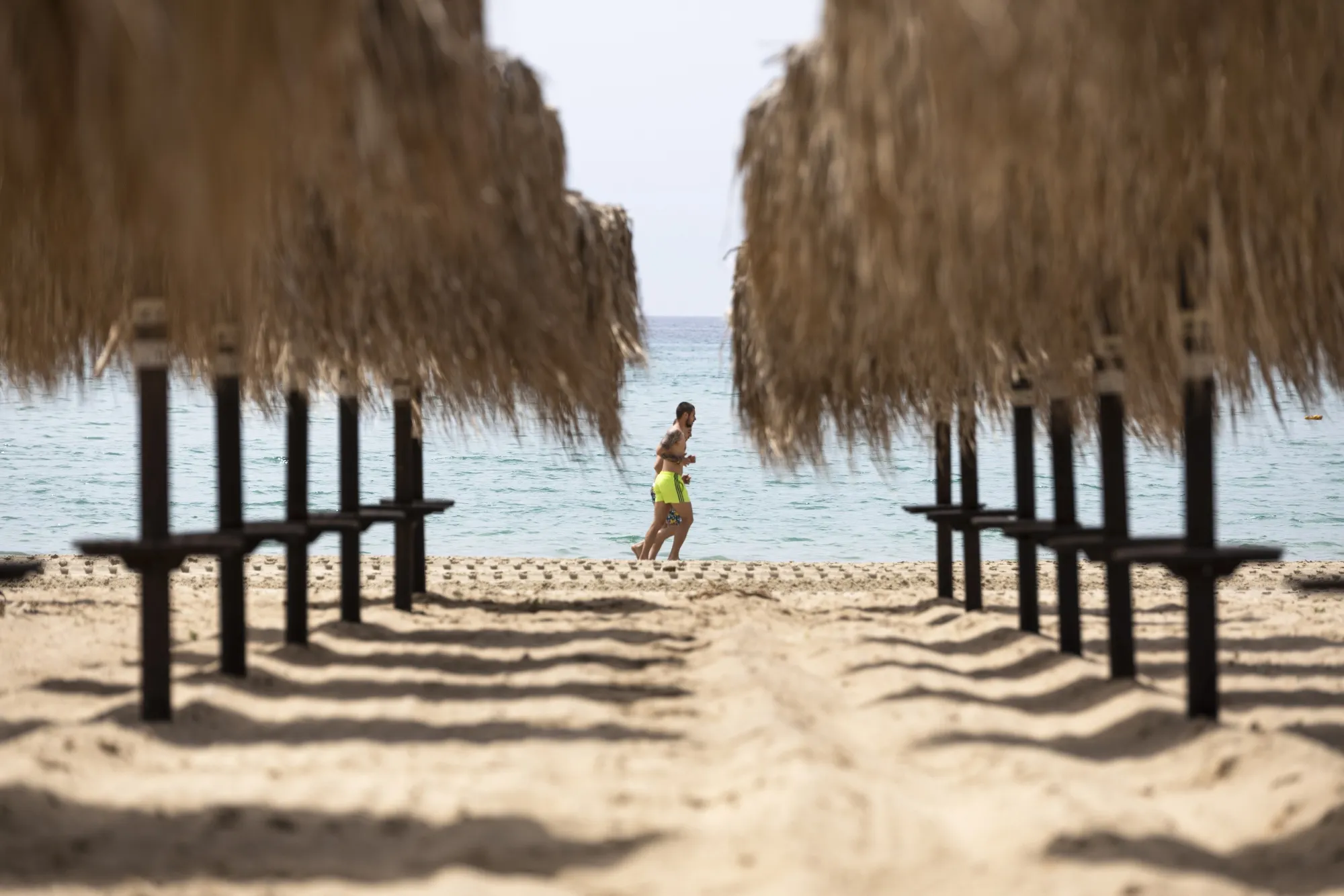 Joggers pass by beach umbrellas in front of a temporarily closed beach bar in Nea Iraklia, Halkidiki, on May 14.