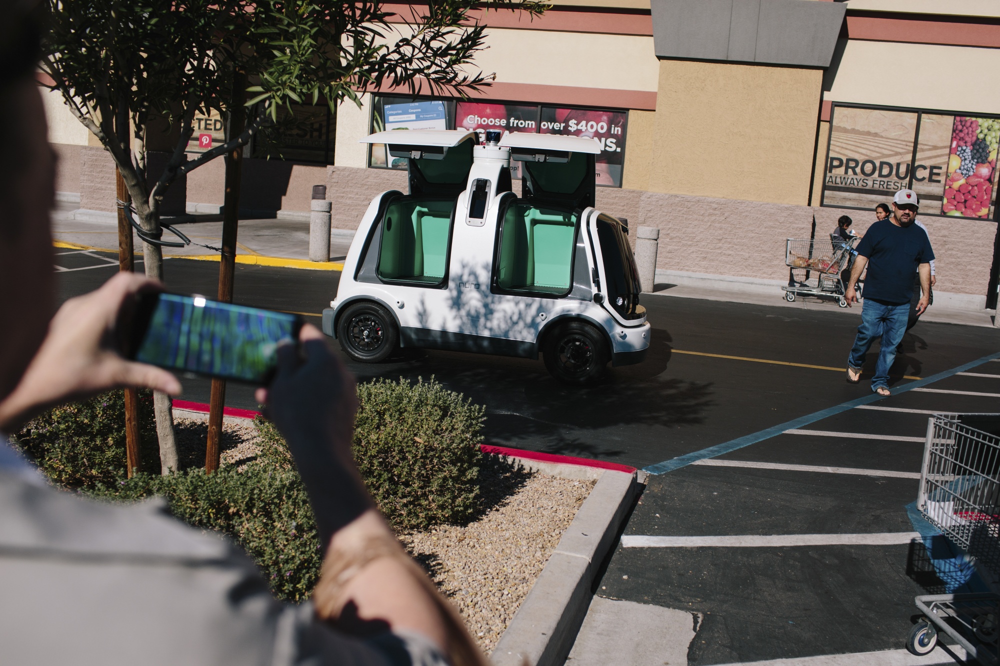 Shoppers photograph a Nuro mini car, which is a self-driving vehicle, outside Fry's Food Store in Scottsdale, Ariz.